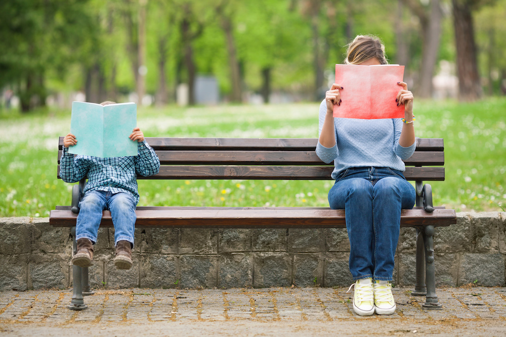 Little boy and his mother sitting on a park bench reading books