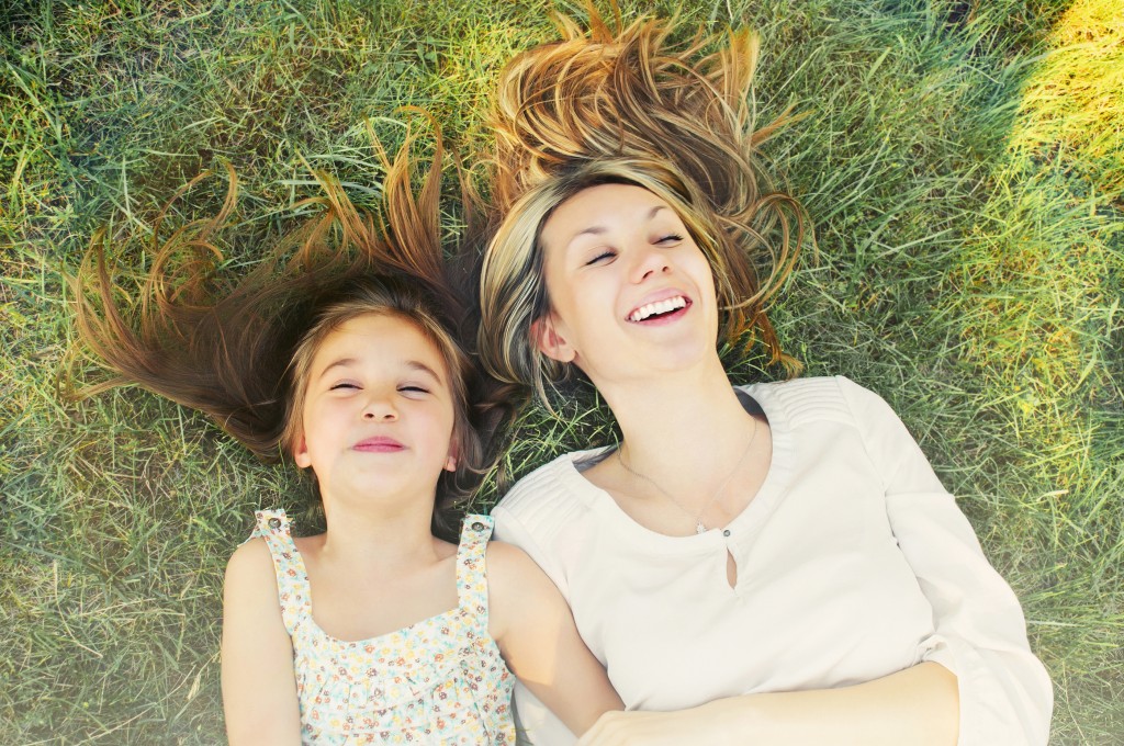happy little girl and her mother having fun outdoors on the green grass in sunny summer day